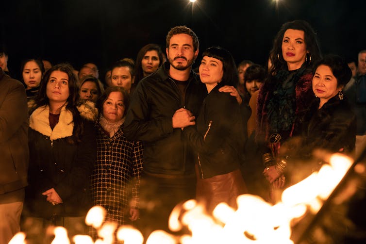 Movie still, people gathered around a bonfire.