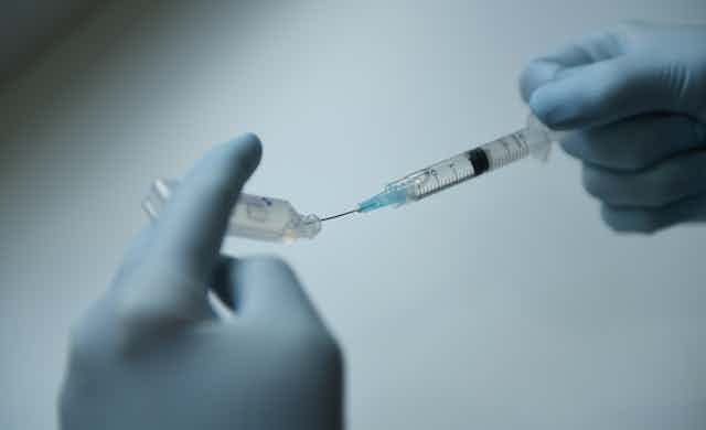 Gloved hands filling a syringe from a vial