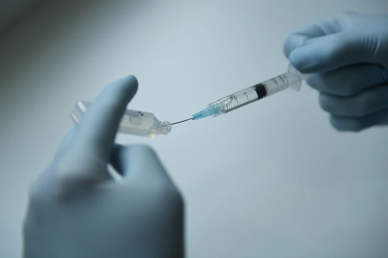 Gloved hands filling a syringe from a vial