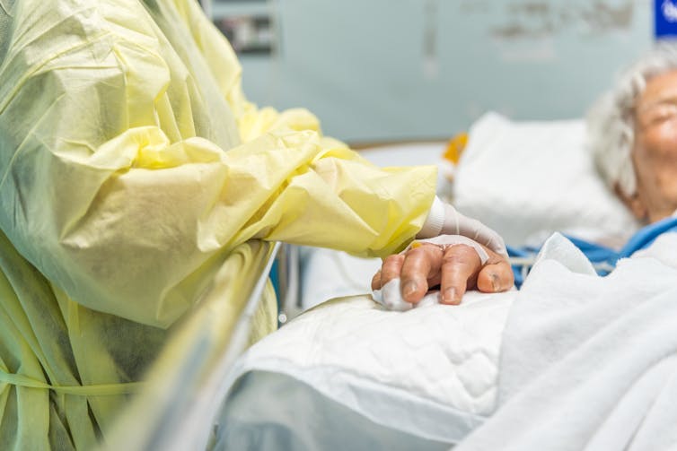 Health-care worker wearing yellow PPE attends to unconscious patient.