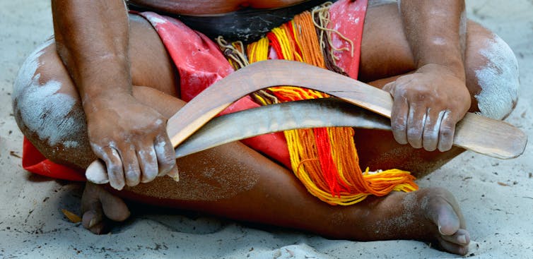 Yugambeh man sitting on the ground holding a boomerang.