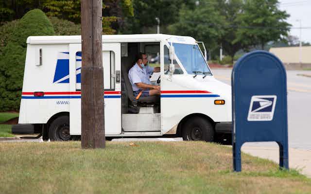 A US postal service worker in van alongside mailbox