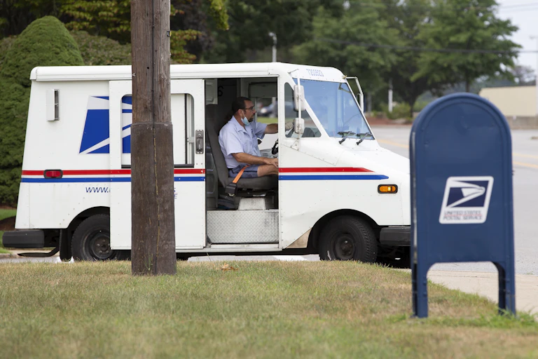 A US postal service worker in van alongside mailbox