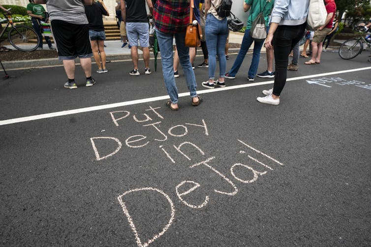 Protestors write 'put DeJoy in DeJail' on path outside DeJoy's apartment.