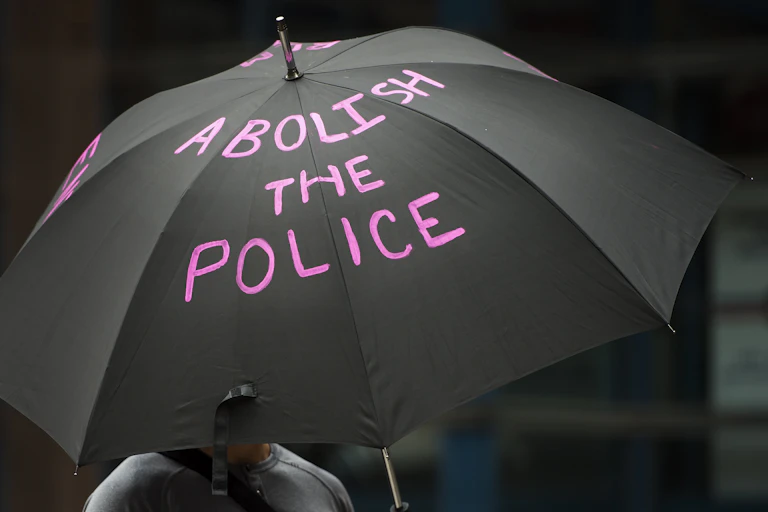 a photograph of someone holding a black umbrella with the words "abolish the police" in pink letters