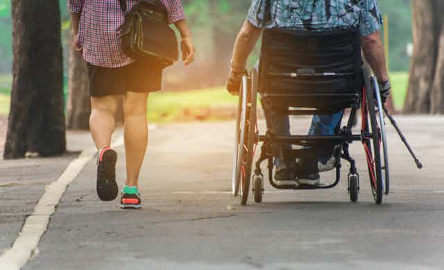 Dos personas de espaldas, una de ellas en silla de ruedas, pasean por un parque.