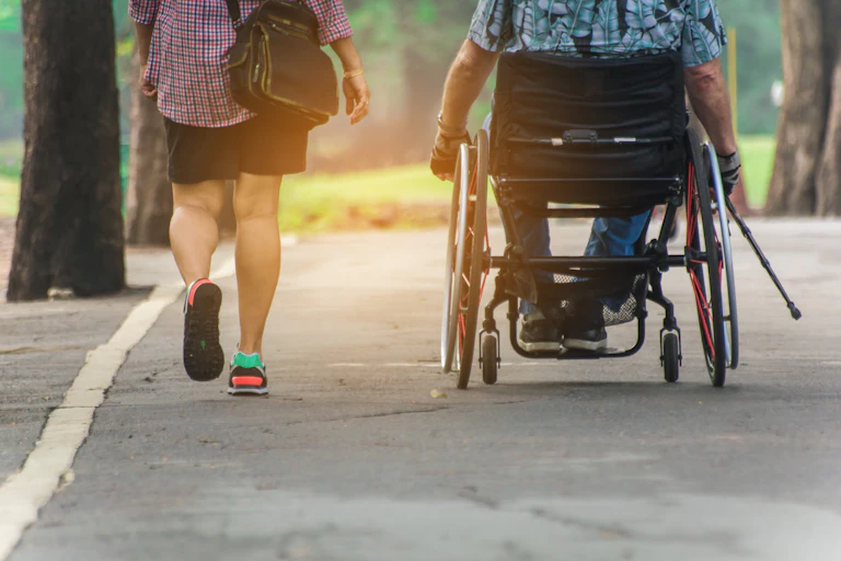 Dos personas de espaldas, una de ellas en silla de ruedas, pasean por un parque.