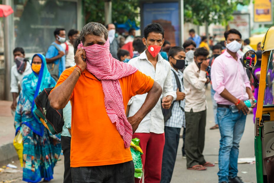 Migrant workers in India stand in the street wearing face masks.