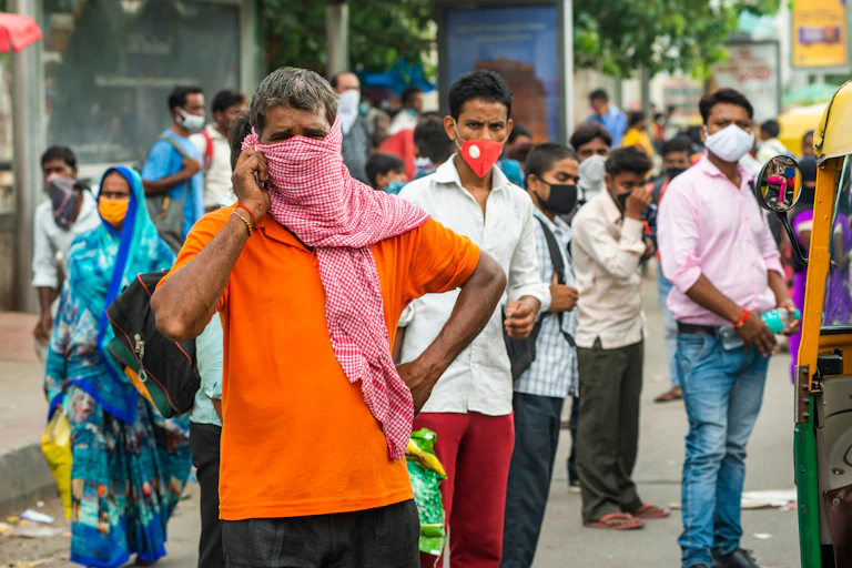 Migrant workers in India stand in the street wearing face masks.