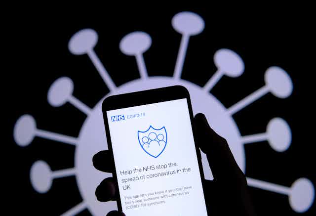 Hand holding smartphone displaying contact tracing app with virus image in background