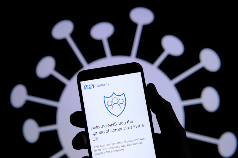 Hand holding smartphone displaying contact tracing app with virus image in background