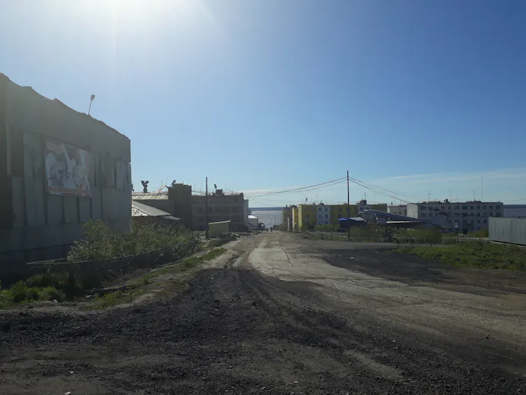 Buildings sit to either side of a road under a blue sky.