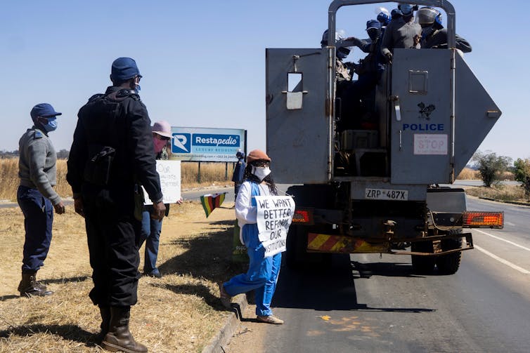 Two women holding placards get into a military vehicle as policemen usher them.