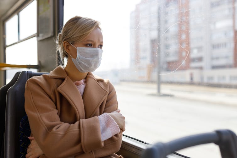 A woman in a surgical mask looks out of a train window