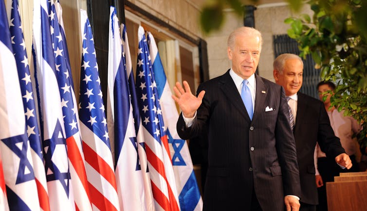 Biden waves next to an array of Israeli and US flags as Netanyahu walks behind him