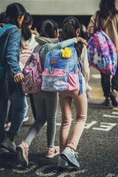 two girls wearing backpacks with their arms around each other