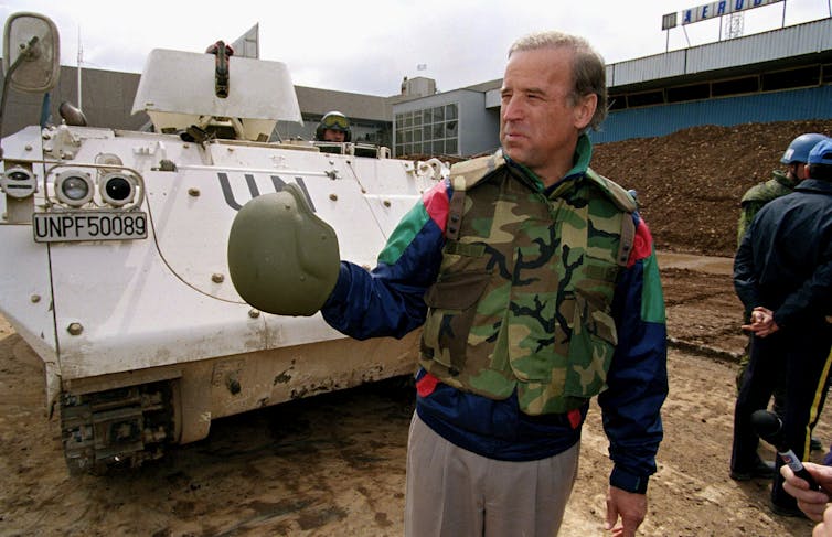 Joe Biden in Bosnia wearing camouflage and standing near a tank