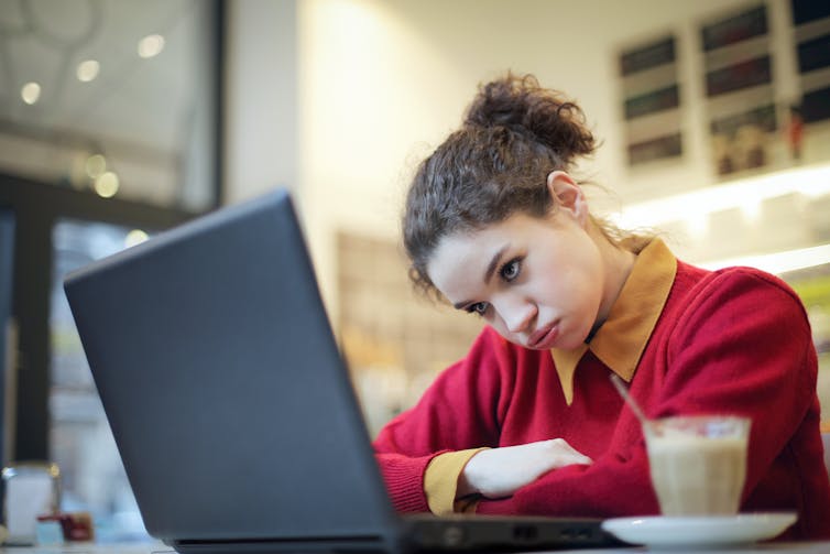 Student with coffee staring in confusion at laptop screen.