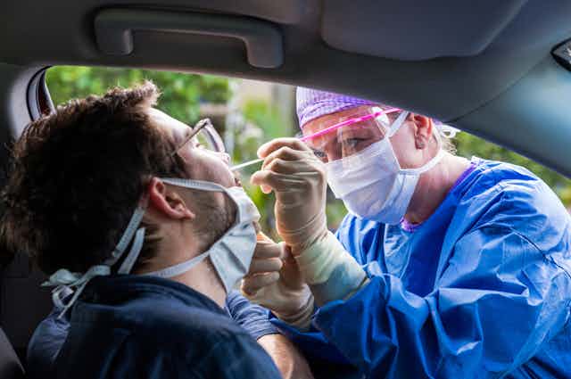 Healthcare worker taking a nasal swab from man sitting in car