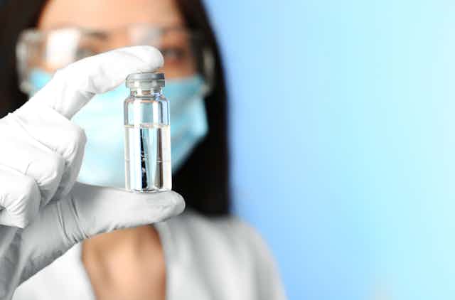 Scientists or doctor wearing masks and gloves holding up a vial of vaccine or medicine.