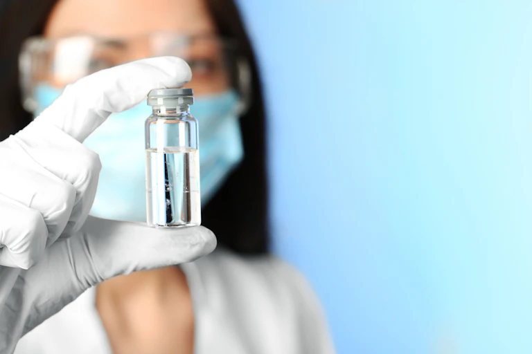 Scientists or doctor wearing masks and gloves holding up a vial of vaccine or medicine.