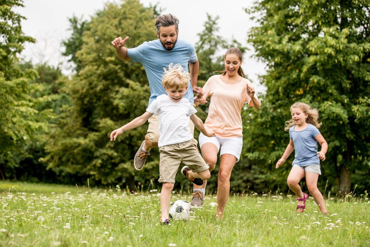 A family (dad, mum, son and daughter) playing soccer in a field.
