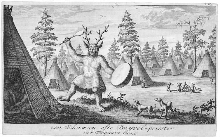 A man dressed as a shaman with a stag antler headdress playing a drum.