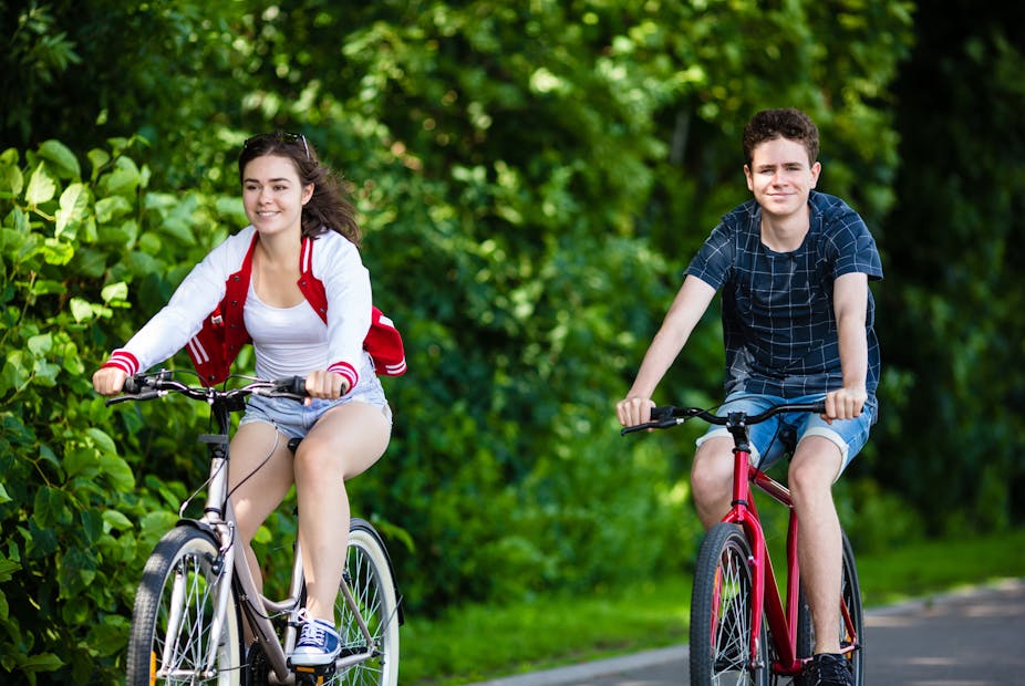 Teen girl and boy riding bicycles in a park.