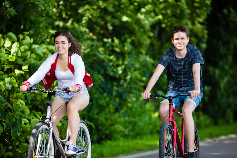 Teen girl and boy riding bicycles in a park.