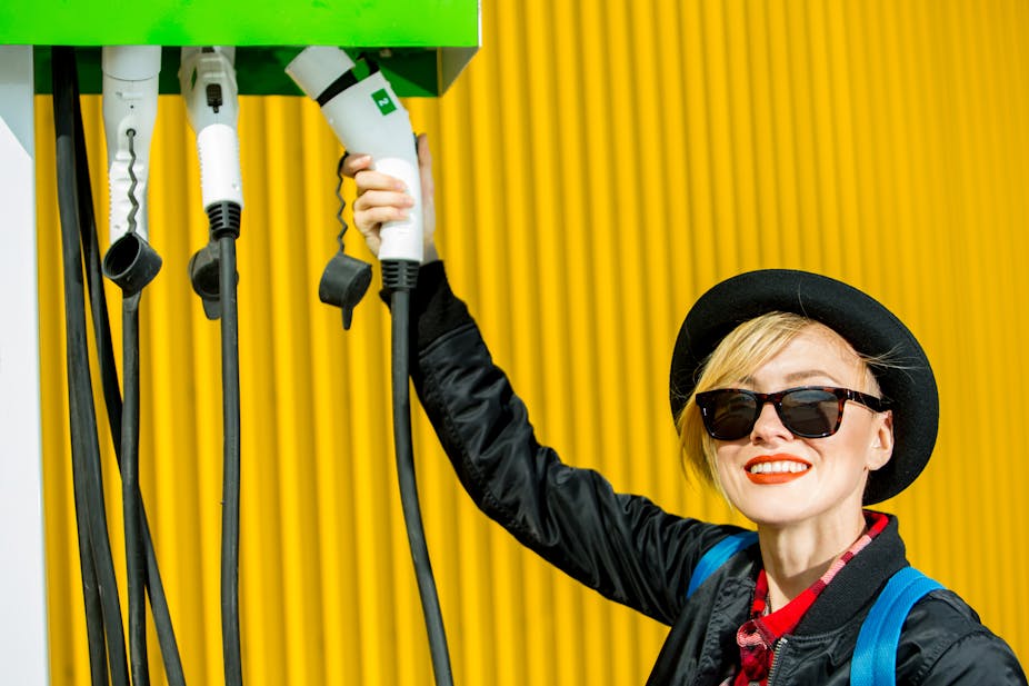 Smiling woman holding electric vehicle charger.