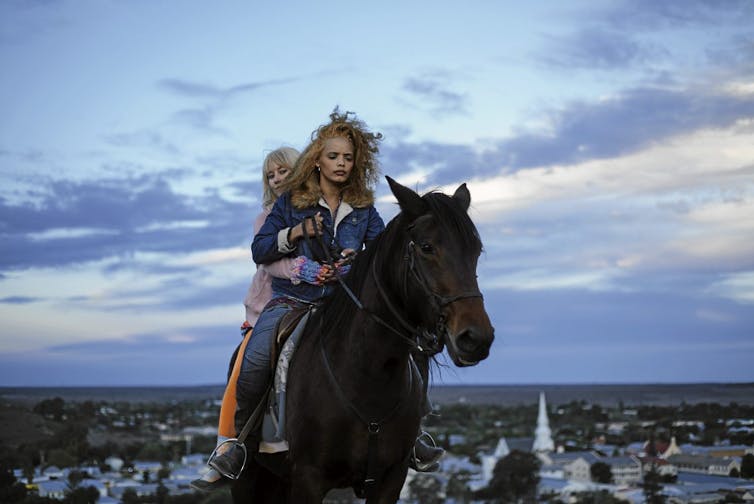 Two young women on a horse riding away from a small South African town.