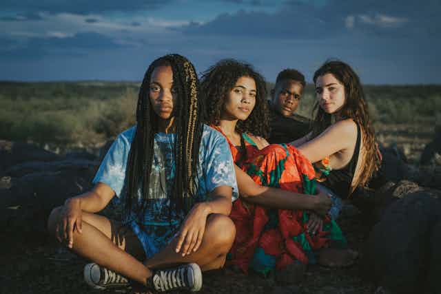 Four young people sit in the open veld looking directly at the camera.