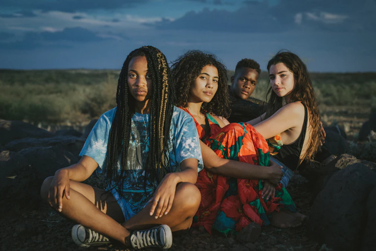 Four young people sit in the open veld looking directly at the camera.