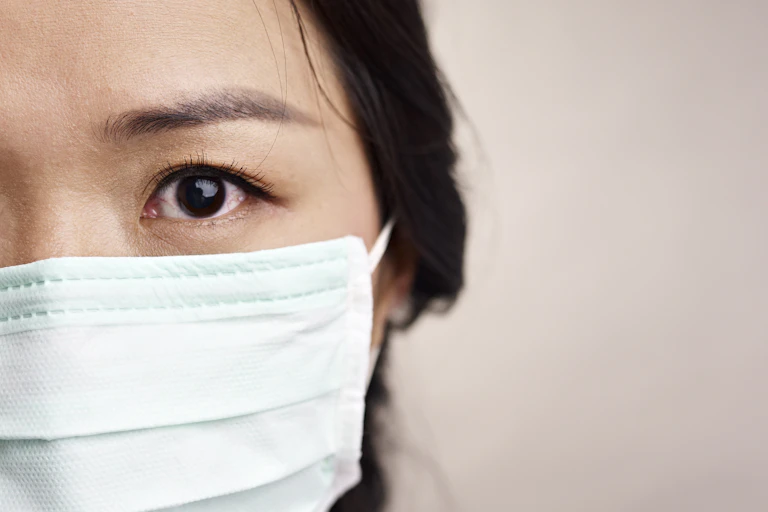 Close-up of the left side of a woman's face wearing a face mask. Her eye is bloodshot.