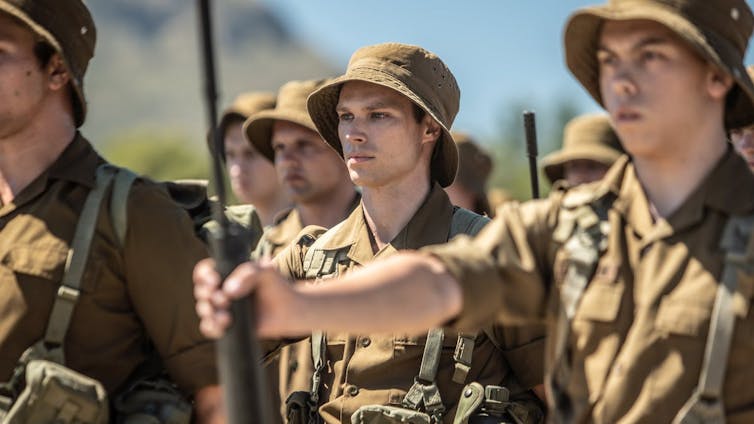 Soldiers stand in formation, holding out their rifles.