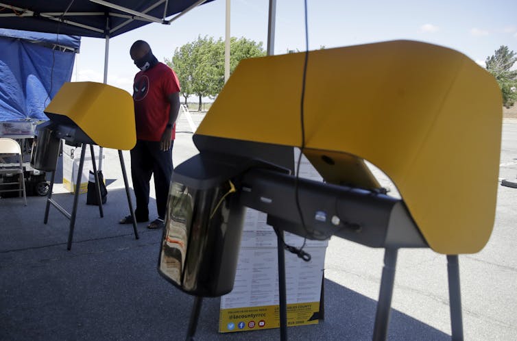 A man stands at an outdoor voting booth.