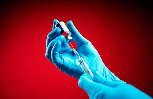 Doctor drawing a vaccine out of a vial with syringe while wearing blue gloves.