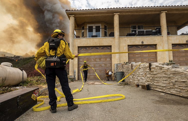 A firefighter holding a hose as he prepares to fight a fire at a burning building.