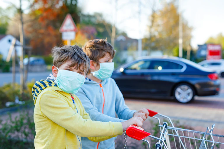 Dos hermanos muy parecidos con mascarillas empujan un carro de supermercado.