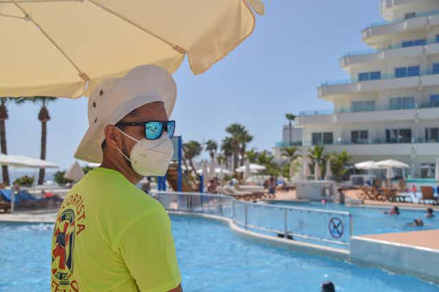 Un socorrista de piscina, con sombrero, mascarilla y gafas de sol.
