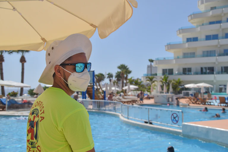 Un socorrista de piscina, con sombrero, mascarilla y gafas de sol.