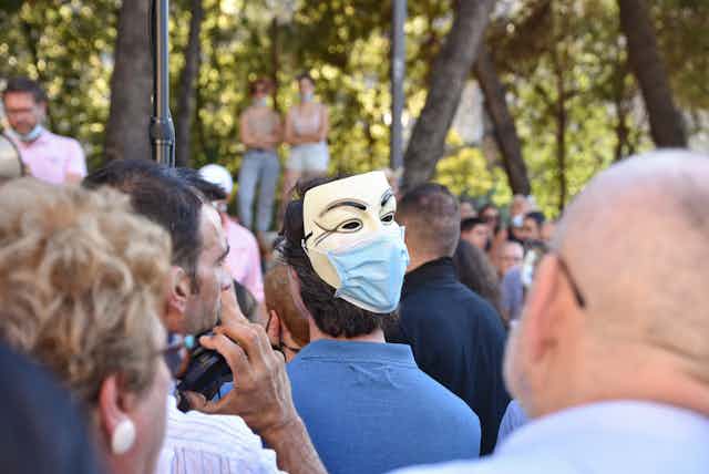 Un hombre porta una máscara de Anonimous con mascarilla quirúrgica.
