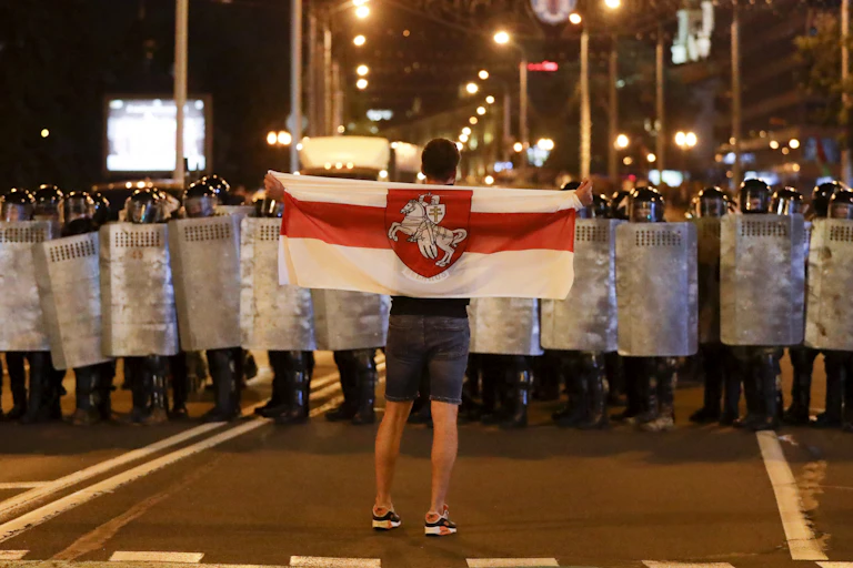 A sole man holding the Belarussian flag faces a line of police in riot gear