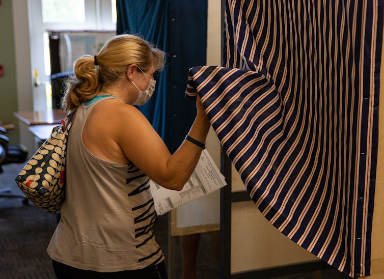 A women pulls back a curtain to enter a voting booth.