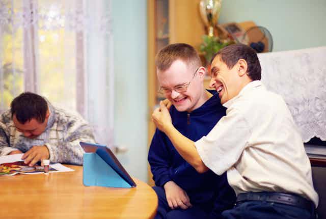 Two men with intellectual disability laughing while watching an iPad.