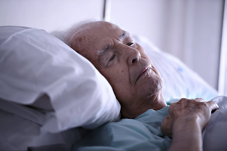 Elderly man lies resting in bed.