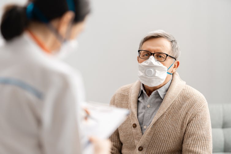 An elderly gentleman wearing a mask is attended to by a nurse.
