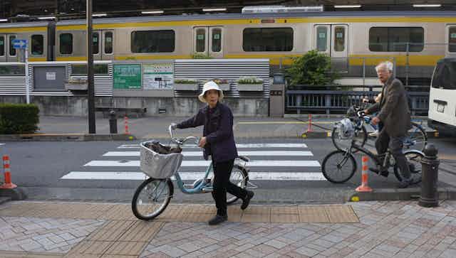 People on bicycles near a railway line in a Japanese city.