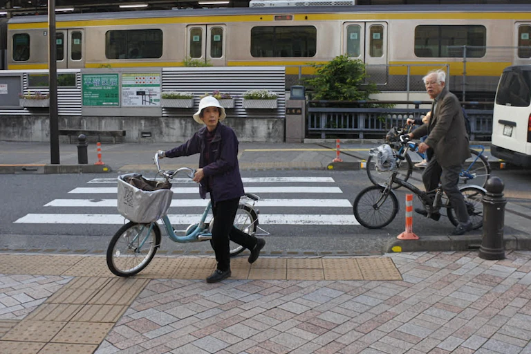 People on bicycles near a railway line in a Japanese city.