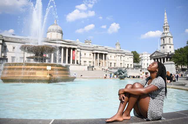 A woman sits beside a fountain in sunny London.